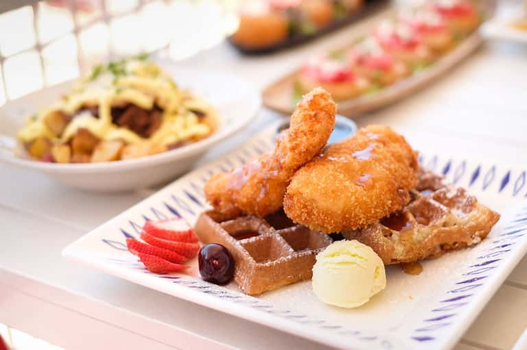 Gourmet dessert plate with fried chicken, waffle, fresh fruit, and ice cream on white china