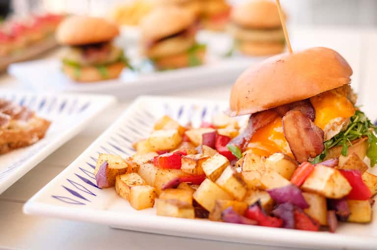 Gourmet burger and crispy potatoes served on white plate with appetizers in background