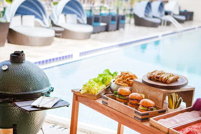 Poolside food service with burgers, wraps, and salads on wooden table near resort pool