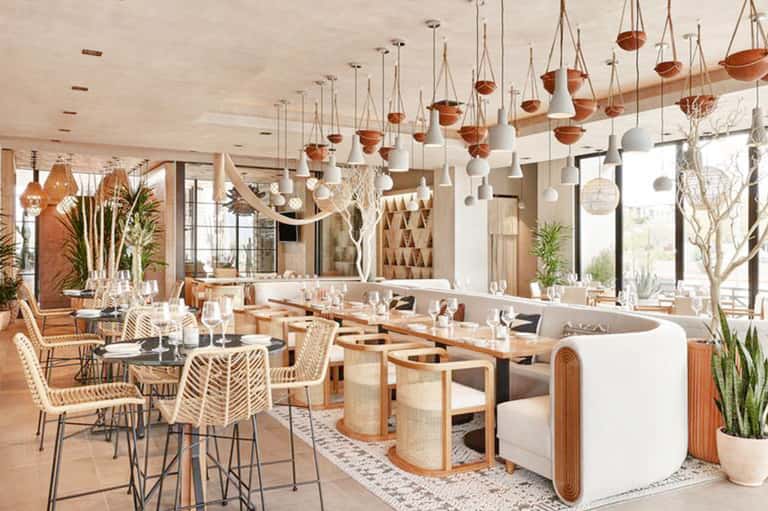 Modern restaurant interior with hanging pendant lights, wooden furniture, and contemporary coastal design