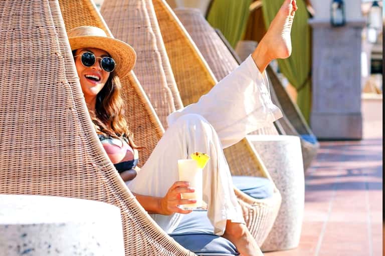 Woman relaxing in wicker beach chair wearing hat and sunglasses with cocktail