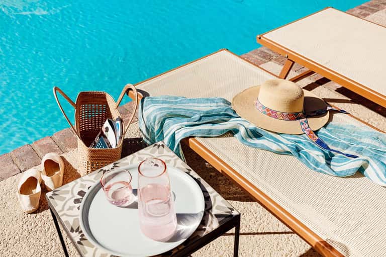 Poolside loungers with towels, hat, and drinks on sunny day beside turquoise water