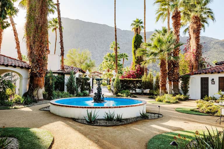 Round blue fountain in desert courtyard surrounded by white Spanish-style buildings and tall palm trees
