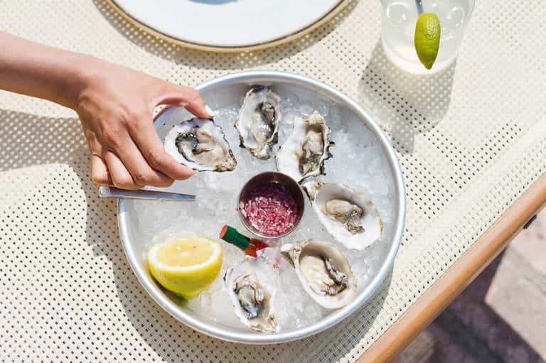 Fresh oysters on ice plate with lemon and pink cocktail sauce at outdoor dining table
