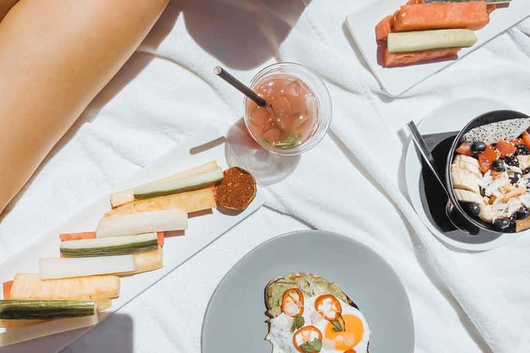 Overhead view of gourmet meal with cocktail, appetizers, and fresh vegetables on white surface
