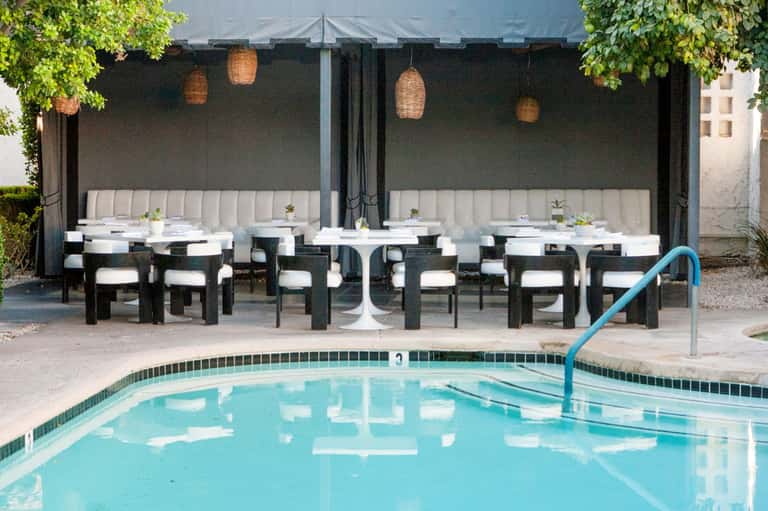 Resort pool with elegant dining cabanas, cream seating, and black umbrellas