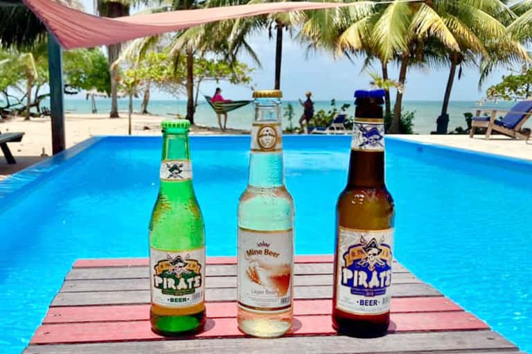 Tropical beach bar with blue pool, palm trees, hammock, and colorful beers served on wooden deck