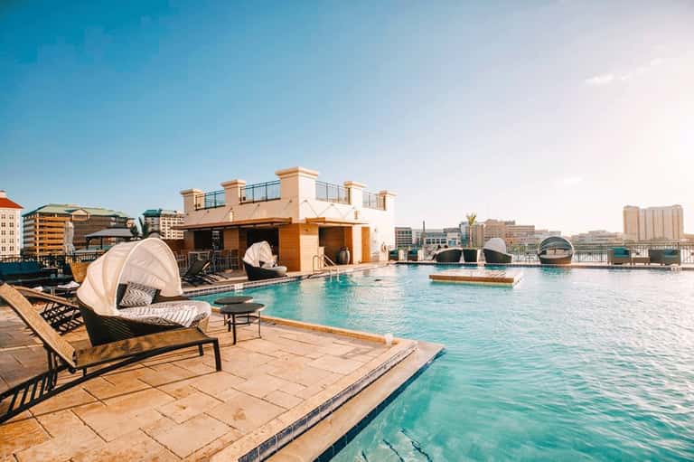 Rooftop pool deck with turquoise water, lounge seating, white cabanas, and city skyline views