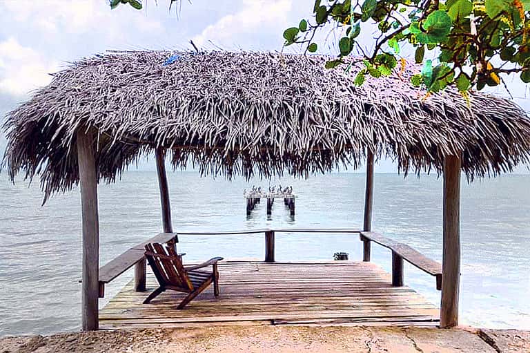 Thatched-roof beachfront pavilion with wooden deck, Adirondack chairs, and ocean view