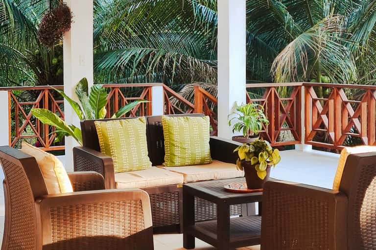 Tropical terrace lounge with wicker furniture, yellow pillows, palm trees, and wooden railings