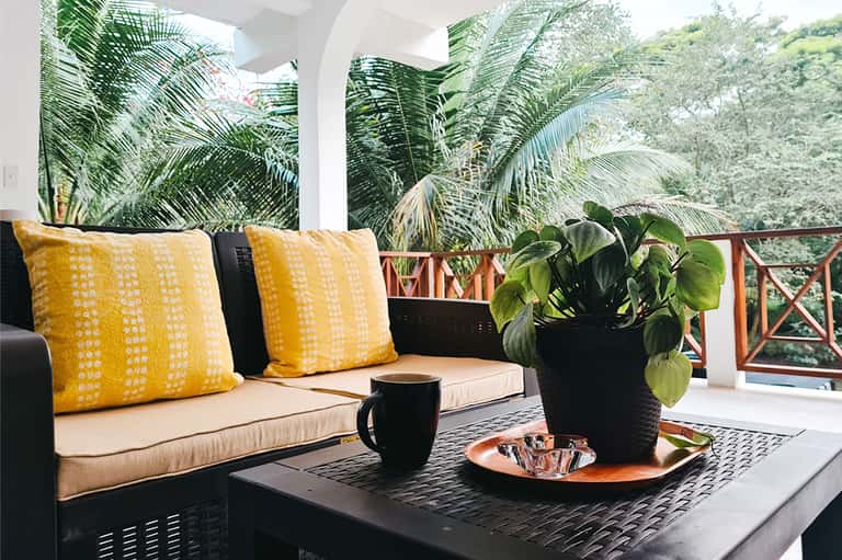 Tropical patio with yellow pillows, black sofa, coffee cup, and lush palm plants