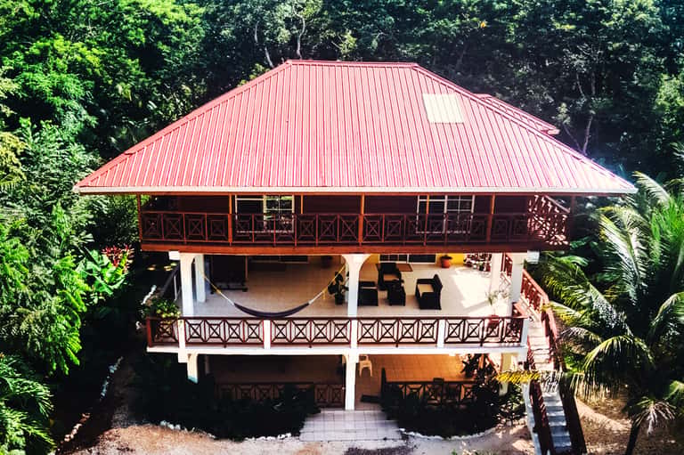 Tropical resort gazebo with red metal roof and wooden railings surrounded by lush greenery