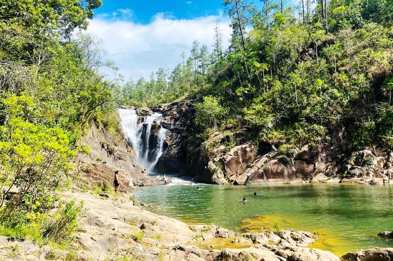 Scenic waterfall cascading into emerald pool surrounded by dense forest and rocky cliffs