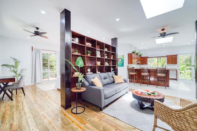 Modern resort living room with gray sofa, wooden shelving, and open kitchen area