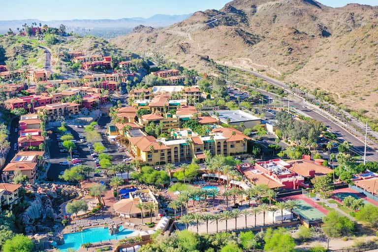 Aerial view of desert resort nestled in mountains with red-tiled buildings and pools