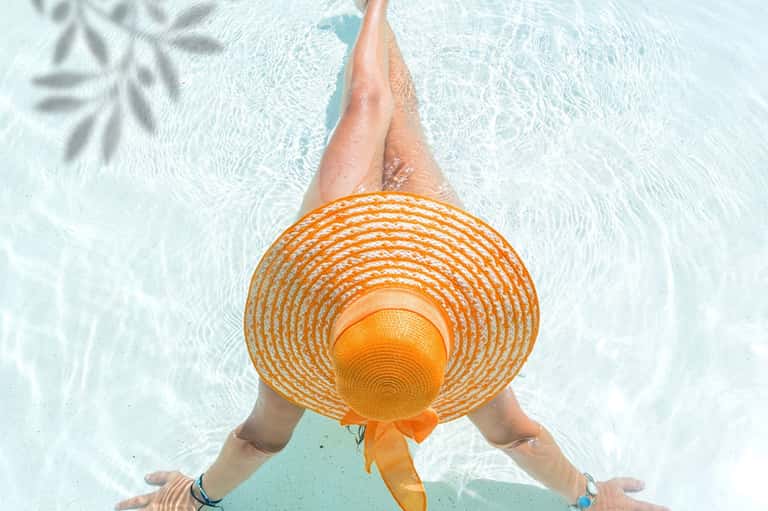 Woman in shallow pool wearing orange straw hat, viewed from above