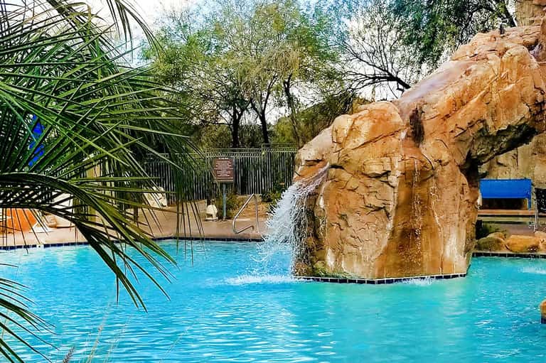 Resort pool with natural rock waterfall feature, palm trees, and lounge chairs