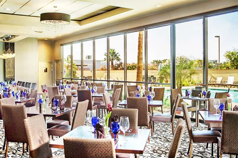 Upscale dining room with floor-to-ceiling windows overlooking pool and palm trees