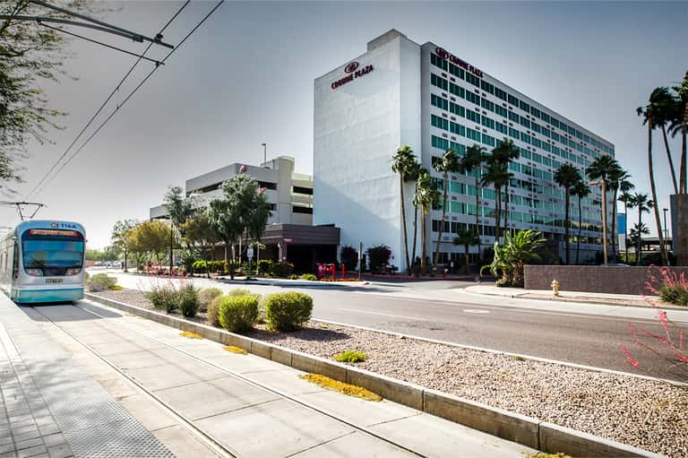 Crowne Plaza hotel exterior with multi-story white building, palm trees, and transit bus on street