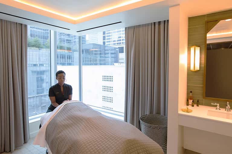 Spa therapist performing massage treatment in modern high-rise hotel room with city views