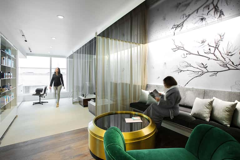 Modern hotel suite with floor-to-ceiling windows, separate living area with green velvet chairs, and workspace