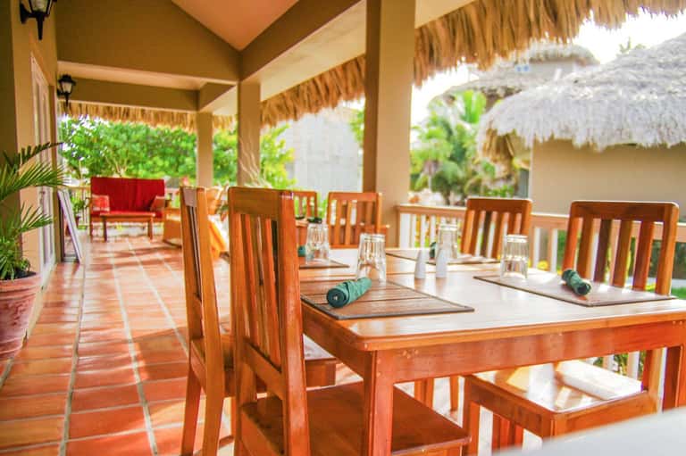Covered dining area with wooden tables and chairs overlooking tropical gardens and ocean