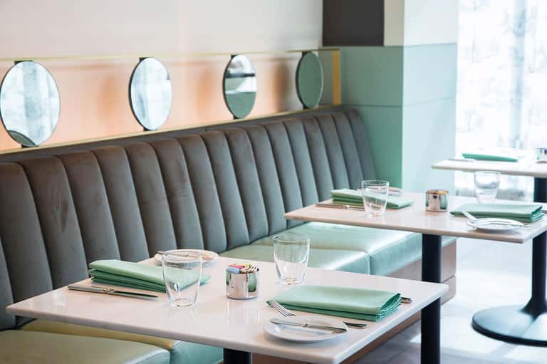 Modern restaurant dining area with gray upholstered booth seating and round mirrors on wall