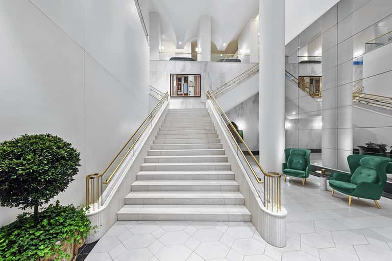 Modern white staircase with gold railings and green seating area in luxury hotel lobby