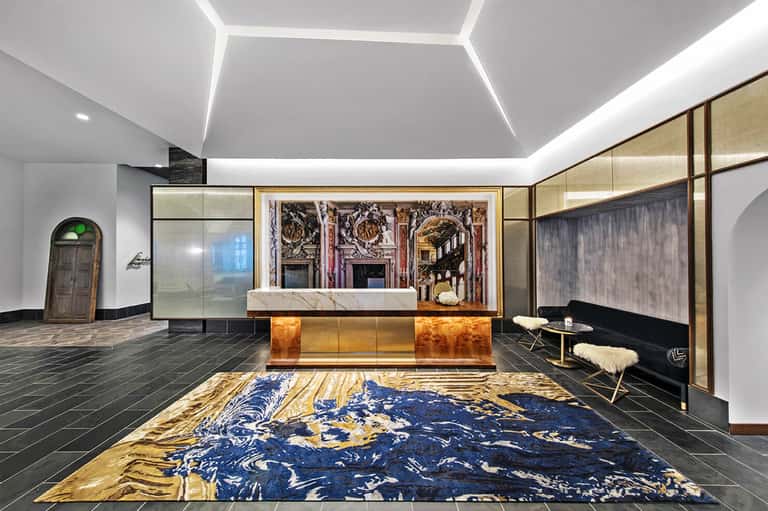 Luxury hotel lobby with marble reception desk, geometric ceiling, and decorative blue and gold rug