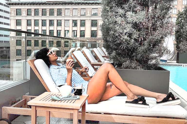 Person relaxing on rooftop lounger with turquoise pool and urban buildings in background