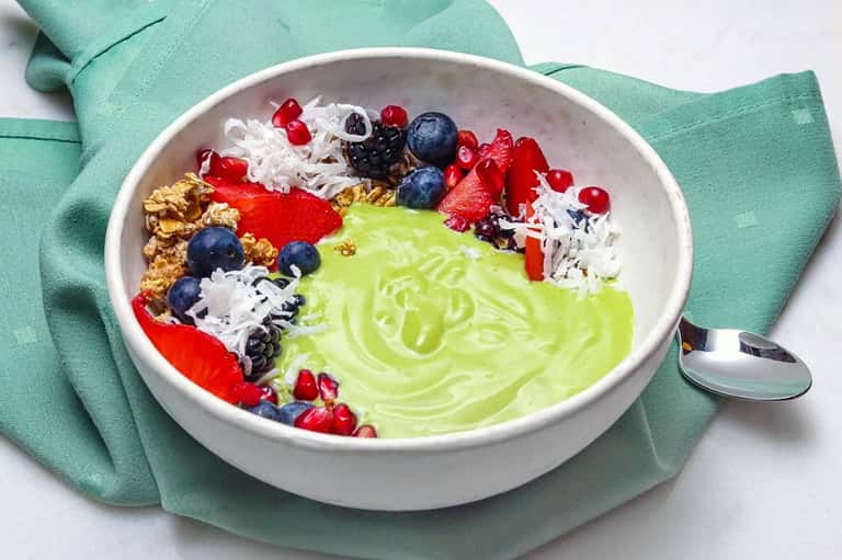 Lime green smoothie bowl topped with granola, berries, and shredded coconut