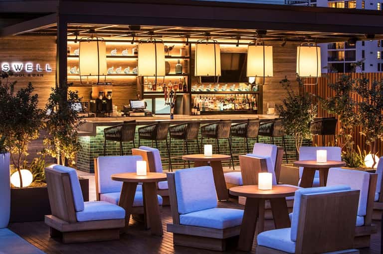 Upscale outdoor pool bar at night with illuminated signage and blue seating areas