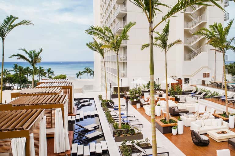 Beachfront resort terrace with lounge chairs, palm trees, and ocean view