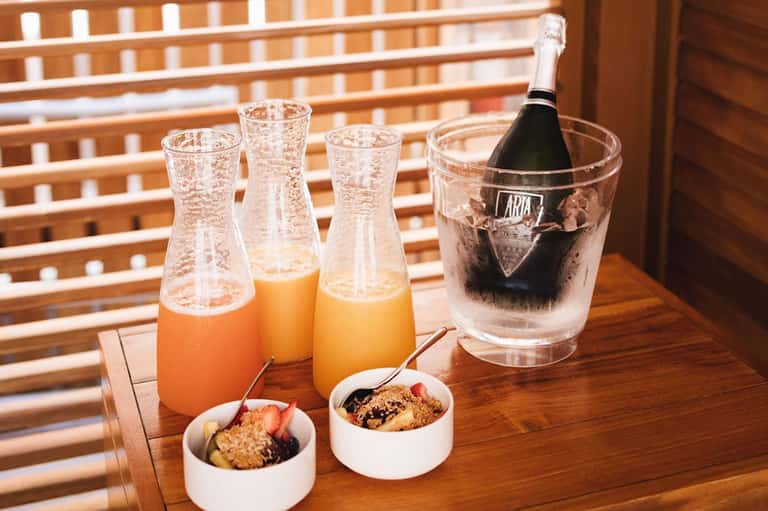Champagne bottle in ice bucket with juice glasses and breakfast bowls on wooden table