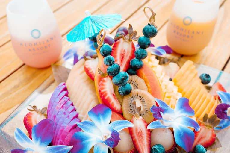 Colorful fruit platter with strawberries, kiwi, blueberries, tropical flowers and cocktails on wooden deck