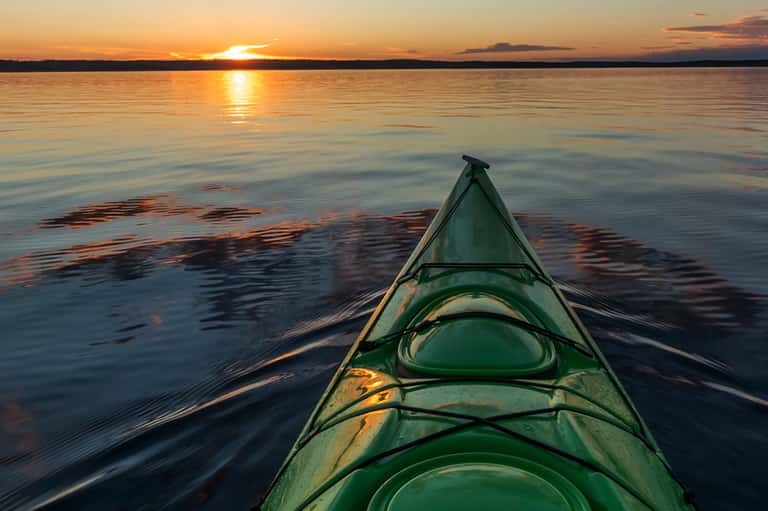 Green kayak on calm water at sunset with golden light reflecting on surface