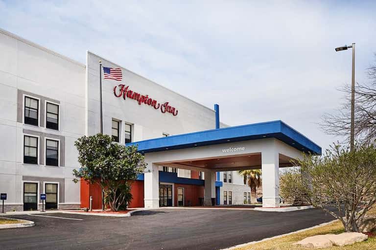 Hampton Inn hotel exterior with white and blue awning, American flag, and welcoming entrance