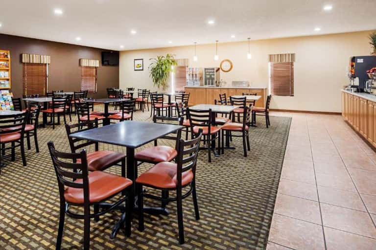 Hotel breakfast room with black chairs, coral cushions, and wooden counter service area