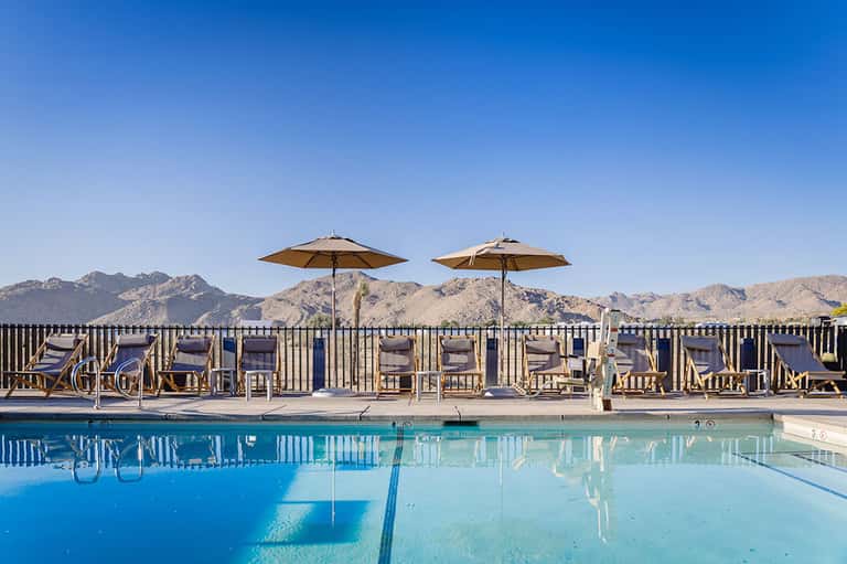 Resort pool with lounge chairs and umbrellas overlooking desert mountains under clear blue sky