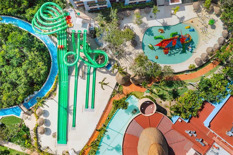 Aerial view of a colorful water park with green slides, lazy river, and multiple pools
