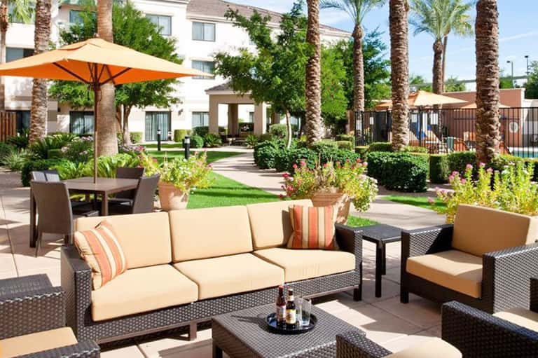 Resort courtyard with comfortable seating, orange umbrellas, palm trees, and lush landscaping