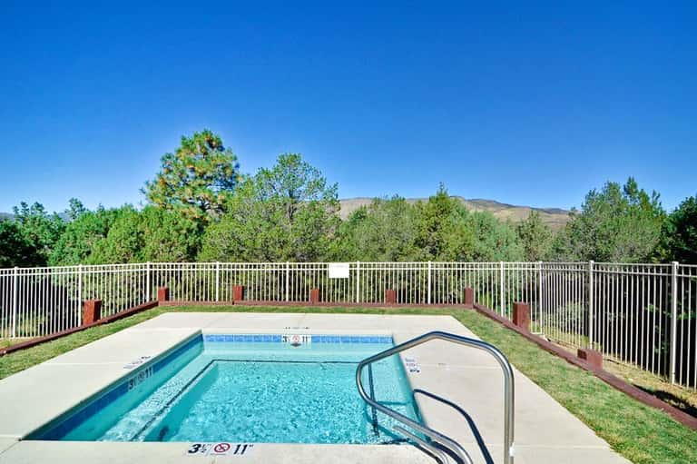 Outdoor swimming pool with white safety railing surrounded by green trees and mountains