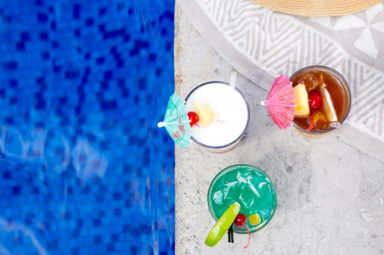 Overhead view of three colorful tropical cocktails by a bright blue pool
