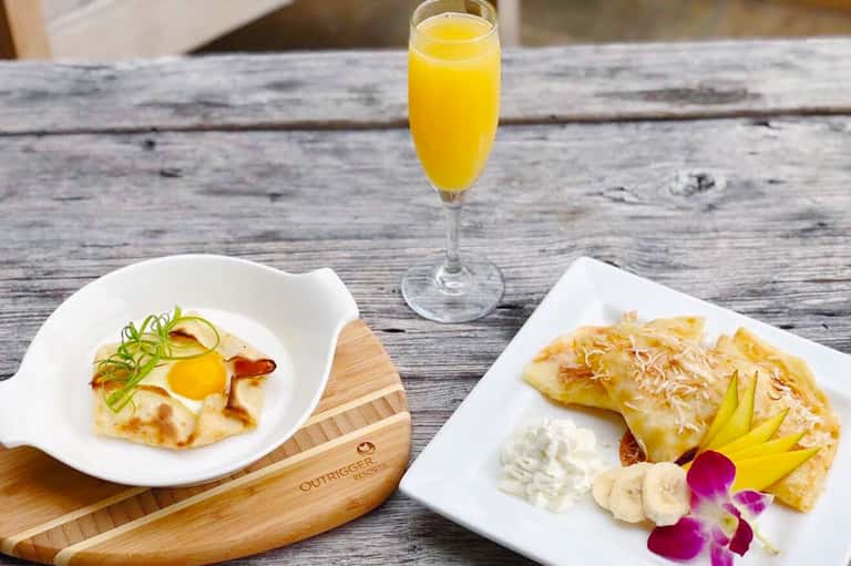 Gourmet breakfast plate with egg dish, pastry, and fresh fruit served with orange juice on wooden table