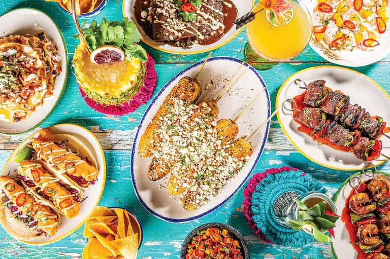 Vibrant overhead view of colorful Mexican dishes and fresh juices on turquoise table