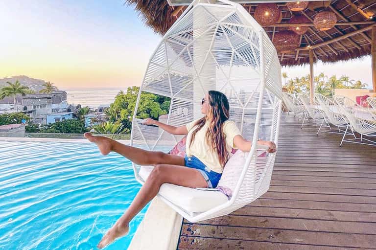 Woman relaxing in white egg chair overlooking ocean and beach at resort at sunset