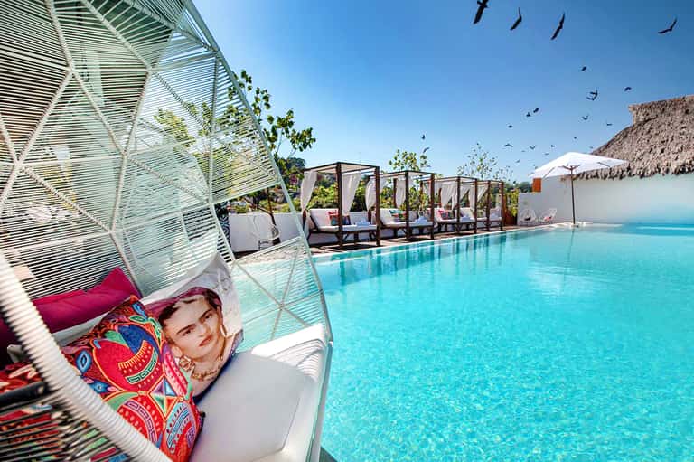 Luxurious resort pool with hanging egg chair, cabanas, turquoise water, and thatched-roof structures