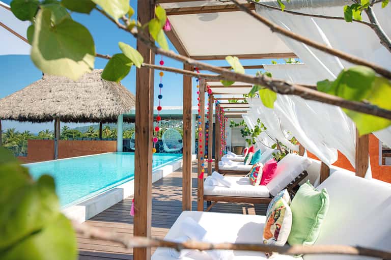 Colorful beachside cabanas with wooden pergola, lounge chairs, and ocean view