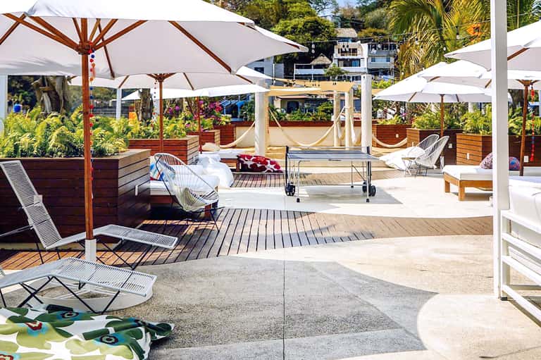 Rooftop lounge area with white umbrellas, wooden deck, and white lounge chairs overlooking water