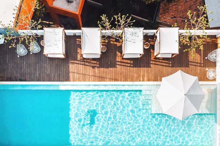Overhead view of pool deck with wooden lounge chairs and white umbrellas beside turquoise pool